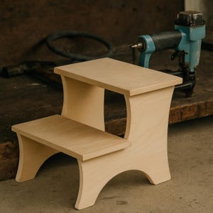 May include: A two-step wooden stool with a natural finish. The stool features a rectangular top and a lower step, supported by curved side panels. The design is simple and functional, suitable for various uses.