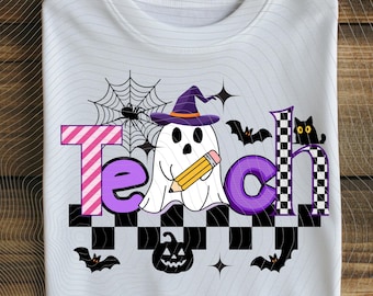May include: White t-shirt with a Halloween-themed graphic. The word "Teach" is spelled out with a pink and purple striped "T", a purple "e", a ghost holding a pencil, and a purple "c" and a checkered "h" with a black cat. Bats, a spider web, and a jack-o'-lantern complete the design.
