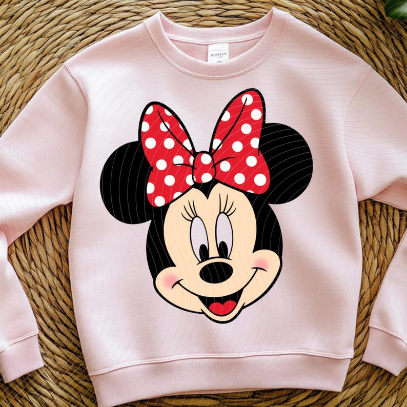 Op de afbeelding: Een lichtroze sweatshirt met een Minnie Mouse-afbeelding. De afbeelding toont Minnie's gezicht met een rode strik met witte stippen. De sweatshirt heeft lange mouwen en een ronde hals.