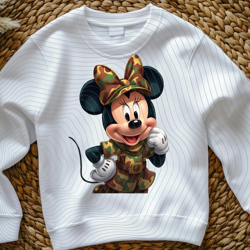 Pode incluir: Uma camisola branca de manga comprida com o gr&aacute;fico de um rato de desenho animado a usar um conjunto com estampado de camuflagem e um la&ccedil;o a condizer. O tecido branco apresenta um padr&atilde;o subtil de linhas horizontais finas e onduladas.