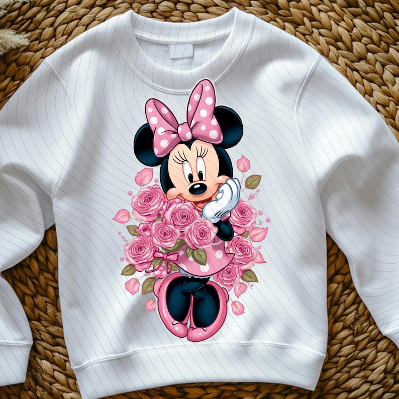 May include: White sweatshirt featuring a Minnie Mouse graphic. Minnie is depicted with a pink polka-dot bow, dress, and holding a bouquet of pink roses. The sweatshirt has a striped pattern.