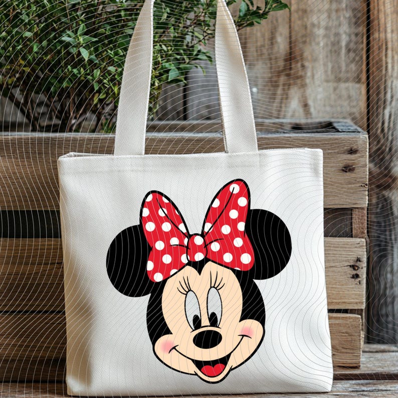 Op de afbeelding: Een witte canvas draagtas met een cartoonafbeelding van Minnie Mouse. De afbeelding toont Minnie's gezicht met zwarte oren, een rode strik met witte stippen en een glimlachende uitdrukking. De tas heeft twee witte handvatten.