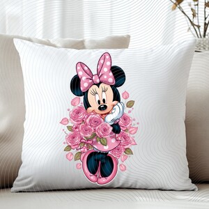 May include: White square throw pillow featuring a cartoon illustration of Minnie Mouse holding a bouquet of pink roses. Minnie Mouse is wearing a pink polka dot dress and bow. The pillow is on a white sofa.