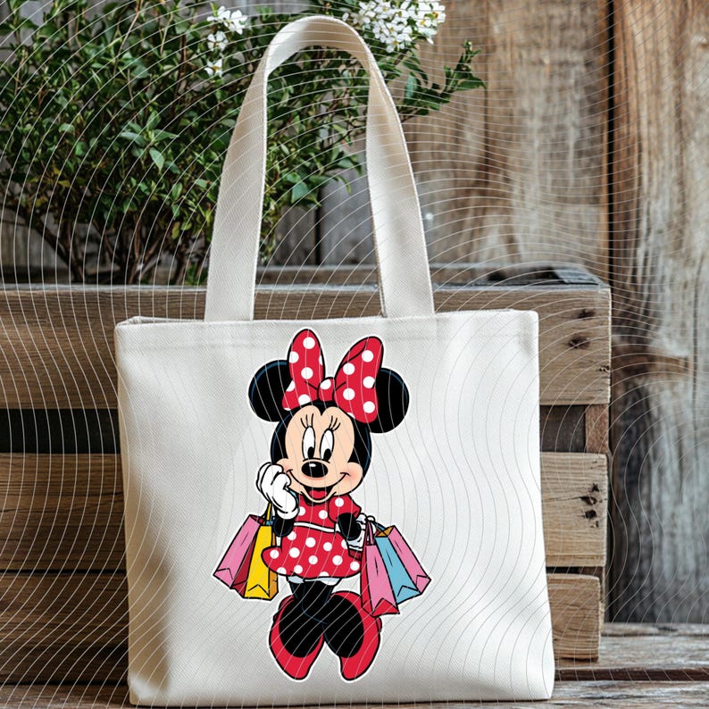 May include: A white canvas tote bag featuring a cartoon illustration of Minnie Mouse in a red polka-dot dress and bow, holding shopping bags. The bag has a rectangular shape with a handle.