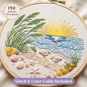 Peut inclure: Un tambour à broder contenant un panneau en tissu avec une scène de plage, un soleil jaune, des vagues bleues, de l'herbe verte, deux petits oiseaux bruns, des coquillages roses et des étoiles de mer. Texte : PDF Pattern Download et Stitch & Color Guide Included.