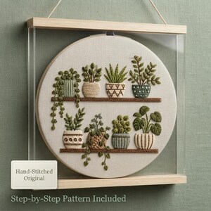 May include: A circular embroidery hoop featuring hand-stitched potted plants on two shelves, encased in a light wood frame. The fabric displays various green botanical designs in textured pots. A small white label reads Hand-Stitched Original.