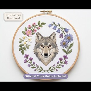 May include: An embroidery hoop containing white fabric with a centered wolf head design surrounded by a floral wreath of pink, white, blue, and purple flowers with green leaves. Text reads PDF Pattern Download and Stitch & Color Guide Included.