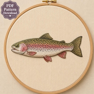May include: A round wooden embroidery hoop containing a fabric panel with a detailed thread-stitched rainbow trout. The fish features green, pink, and cream scales with dark spots. A label in the upper left corner reads PDF Pattern Download.