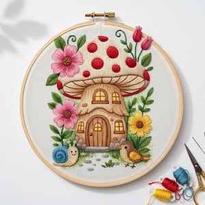 May include: Embroidered mushroom house in a wooden hoop. The whimsical design features a mushroom with red spots, a wooden door, and windows. Pink flowers, a snail, and a bird are also included in the design. The embroidery is set against a white background.