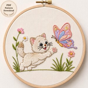 May include: A round wooden embroidery hoop containing a fabric panel with a hand-stitched design of a cream-colored kitten reaching toward a multi-colored butterfly. The scene includes green grass, pink and white flowers, and text reading PDF Pattern Download.