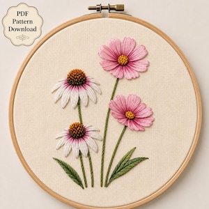 Può includere: Un telaio da ricamo circolare in legno contenente tessuto color bianco sporco con disegni floreali cuciti a mano. Il ricamo presenta due fiori di cosmea rosa e due echinacee bianche con centri marroni, steli e foglie verdi. Il testo recita PDF Pattern Download.