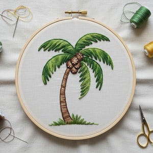 May include: A hand-stitched embroidery of a palm tree in a wooden hoop. The tree features a brown trunk, green fronds, and brown coconuts. Green, yellow, and brown thread spools, a needle, and gold scissors surround the hoop on a white fabric background.