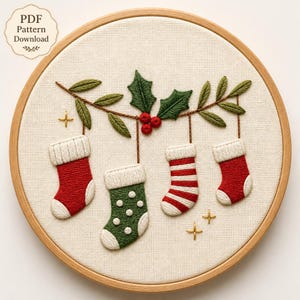 Op de afbeelding: Een ronde borduurring met een stuk stof met een handgeborduurd ontwerp van vier hangende kerstsokken in rood, groen en wit. De sokken hangen aan een groene hulsttak met rode bessen. De tekst luidt PDF Pattern Download.
