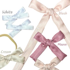 Puede incluir: Surtido de lazos de satén en blanco, rubor, malva y crema. Los lazos están atados con cintas largas y fluidas. La palabra "White" está escrita encima de los lazos blancos, "Blush" encima del lazo rubor, "Mauve" encima del lazo malva y "Cream" encima del lazo crema.