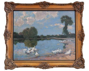 May include: An oil painting of a serene landscape featuring a lake with white geese. The sky is blue with fluffy clouds, and the painting is framed in a decorative, ornate gold frame. The artwork depicts a peaceful rural scene.