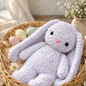 May include: A handmade, white crochet bunny with long floppy ears, black eyes, and a pink nose, resting in a woven basket. The basket contains decorative Easter eggs in pastel colors. A charming Easter-themed decorative item.