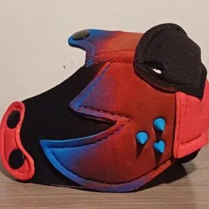 May include: A red, black, and blue pup hood with a rounded ear, nose, and blue spikes. The hood is made of a soft material and has a gradient effect from red to blue. The nose has two black circles.