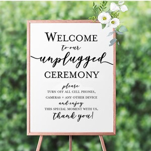 May include: A white sign with a wooden frame on an easel, announcing an unplugged ceremony. The sign reads "Welcome to our unplugged ceremony, please turn off all cell phones, cameras and any other device and enjoy this special moment with us. Thank you!"