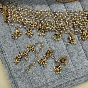 May include: A gold-toned necklace and earring set featuring faux pearls and decorative pendants. The necklace has multiple strands of small pearls and gold chain. The earrings and necklace pendants have a floral design with small pearl accents.