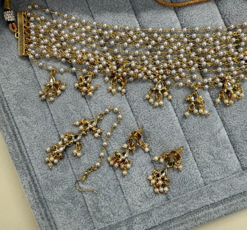 May include: A gold-toned necklace and earring set featuring faux pearls and decorative pendants. The necklace has multiple strands of small pearls and gold chain. The earrings and necklace pendants have a floral design with small pearl accents.