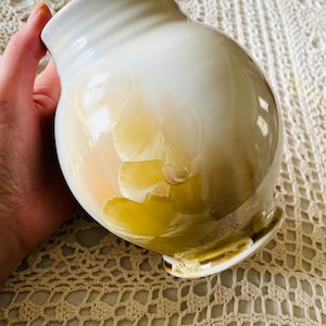 May include: A white ceramic vase with a yellow and orange floral design. The vase has a rounded body and a flared lip.