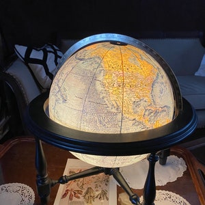 May include: A black globe with a wooden stand and a lit-up map of North America. The globe is sitting on a wooden table with a piece of paper and a doily.