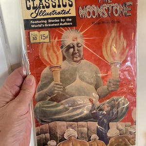 May include: A vintage comic book cover featuring an illustration of a large, blue, seated Buddha figure with a glowing halo. The cover is red and features the title "The Moonstone" and the author "William Wilkie Collins". The comic book is part of the "Classics Illustrated" series, with the number "30" and price "15 cents" printed on the cover.