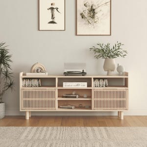Può includere: Mobile TV in legno chiaro con giradischi, libri e oggetti decorativi. Il mobile ha ante a doghe e ripiani aperti. Due opere d'arte incorniciate sono appese sopra. Una pianta in vaso e un tappeto sono in primo piano.