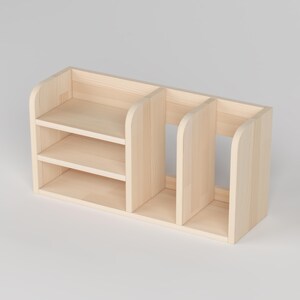 May include: A light-colored wooden desk organizer with three compartments. The organizer has two shelves on the left side and a larger open space on the right. The wood has a natural finish.