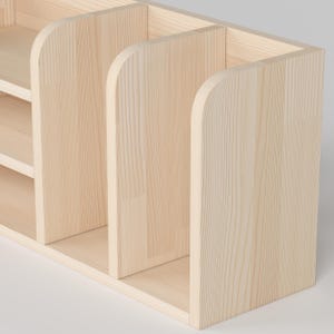 May include: A light-colored wooden organizer with multiple compartments. The organizer has a rectangular base and vertical dividers with rounded tops. The wood grain is visible, and the overall design is simple and functional.