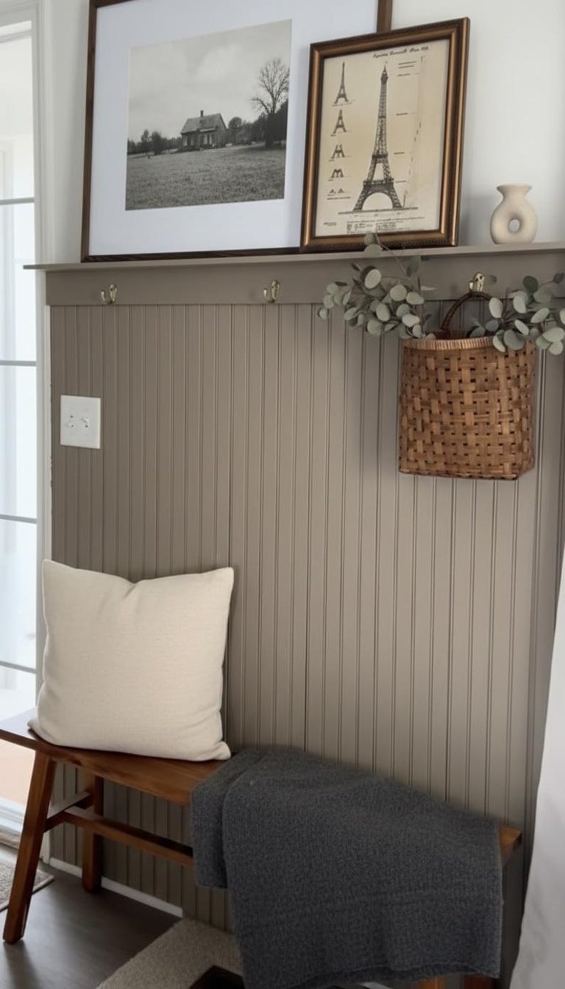 Pu&ograve; includere: Scena d'interni accogliente con una panca in legno, un cuscino color crema e una coperta grigio scuro. Sopra, una foto in bianco e nero incorniciata e una stampa vintage della Torre Eiffel sono appese a una parete grigia a pannelli. Un cesto intrecciato con vegetazione aggiunge un tocco naturale.