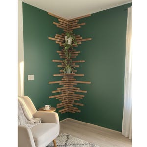 Puede incluir: Estanter&iacute;a esquinera de madera con un dise&ntilde;o geom&eacute;trico &uacute;nico. Los estantes son de madera te&ntilde;ida y est&aacute;n montados en una pared verde oscuro. Dos plantas en macetas se exhiben en los estantes. Un sill&oacute;n de tonos neutros y una peque&ntilde;a mesa auxiliar est&aacute;n en primer plano.