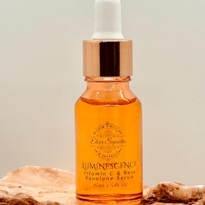 K&ouml;nnte beinhalten: Eine Glasflasche mit Luminescence Vitamin C & Rose Squalane Serum. Die Flasche hat eine Tropferspitze mit einem wei&szlig;en Kolben und einem ros&eacute;goldenen Kragen. Das Serum ist orange und das Etikett lautet "Elixir Sapientia". Die Flasche ist 15 ml.