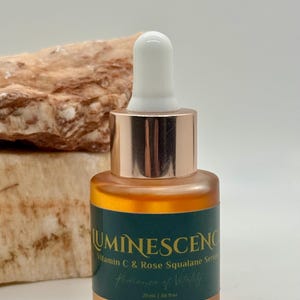 K&ouml;nnte beinhalten: Eine Glasflasche Serum mit wei&szlig;em Tropferaufsatz und kupferfarbenem Kragen. Die Flasche hat ein dunkelgr&uuml;nes Etikett mit dem Wort "LUMINESCENCE" und dem Text "Vitamin C & Rose Squalane Serum". Die Flasche enth&auml;lt 20 ml Serum.
