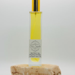 May include: A rectangular glass bottle filled with yellow liquid, topped with a gold-colored cap. The bottle has a label that reads "Elixir Sapientia Skin Apothecary" and "Monoi & Frangipani Indulgent Body Oil."