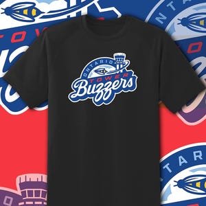 May include: A black short-sleeved t-shirt featuring a graphic on the chest. The graphic displays a blue and white logo with an illustration of a bee and an air traffic control tower, with the text "ONTARIO TOWER Buzzers" printed in blue and red.