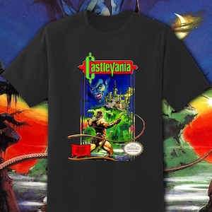 May include: Black t-shirt featuring a graphic from the video game Castlevania. The design includes the game's logo, a character with a whip, a castle, and a vampire. The Nintendo seal of quality is also visible.
