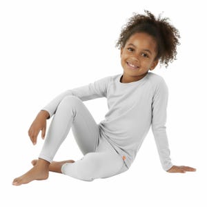 May include: A light gray long-sleeved shirt and matching leggings set. The set is made of a soft, lightweight material. The child is sitting on a white background.