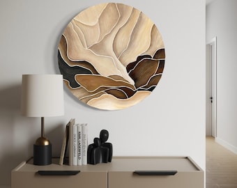 May include: A circular wall art piece featuring an abstract design of layered, flowing shapes in shades of cream, beige, tan, brown, and black. The composition is defined by distinct, curved outlines that separate each color block, creating a topographical effect across the round surface.