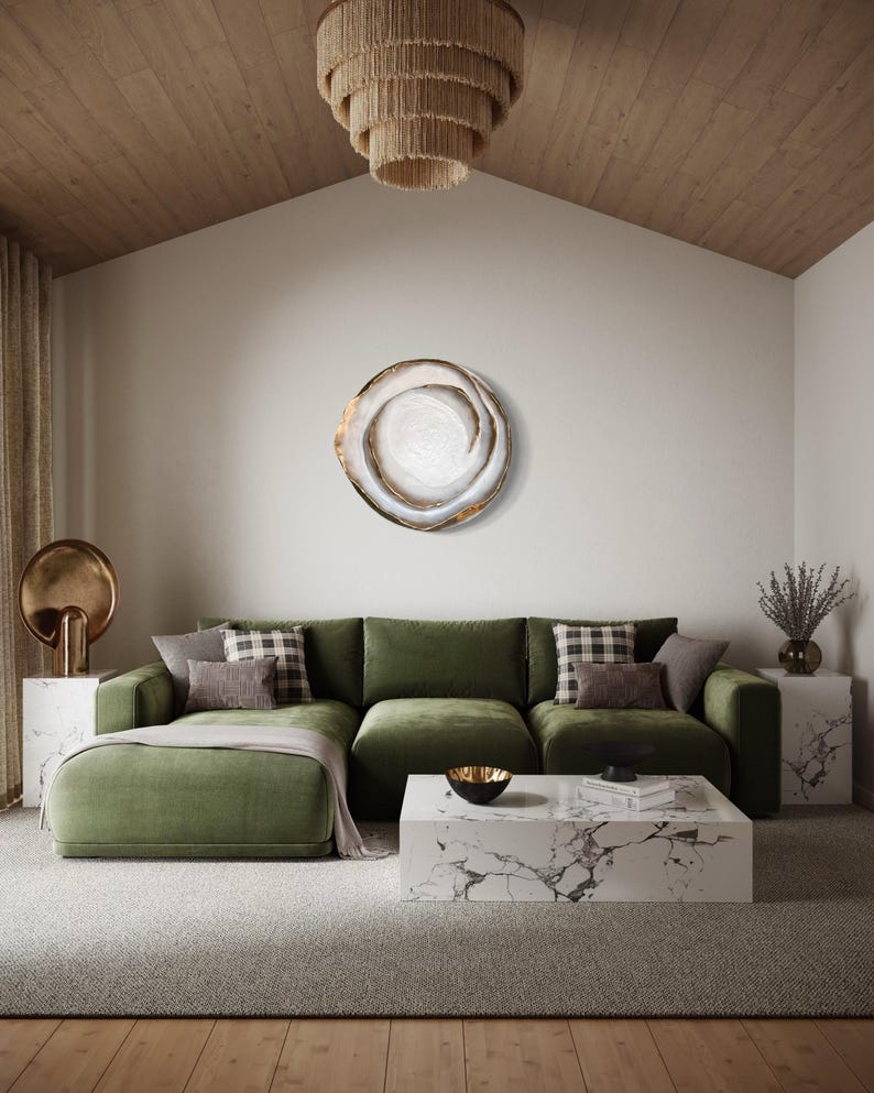 May include: A modern living room with a green sectional sofa, marble coffee table, and a decorative wall art piece. The room features a neutral color palette with a textured rug and a wooden ceiling. A tiered chandelier hangs from the ceiling.