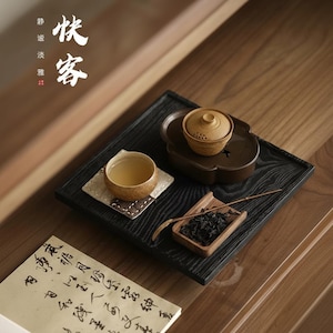 以下が含まれることがあります： 黒い木製のトレイに置かれた伝統的なティーセット。 セットには、お茶が入った小さなセラミックカップ、ティーポット、茶葉が入った小さな木製容器、小さなスプーンが含まれています。