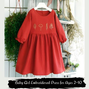May include: A red baby girl's dress with long sleeves and an embroidered floral design. The dress has a round neckline and a gathered skirt. The text at the bottom reads: Baby Girl Embroidered Dress for Ages 2-10.