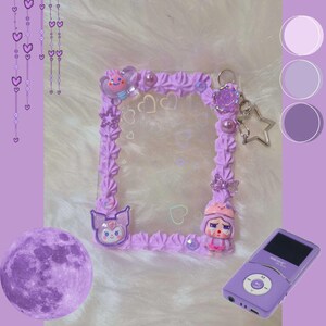 May include: A lavender-colored decorative frame with a clear center, adorned with whimsical embellishments. The frame features a textured, piped design, small charms, and a star-shaped keychain. A purple MP3 player and a purple moon are also in the image.