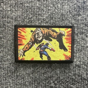 May include: A rectangular embroidered patch featuring a comic book illustration of Captain America in a blue, red, and white suit fighting a large figure in a brown jacket with a black swastika emblem on a bright yellow background with red accents.