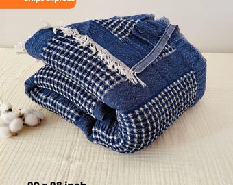 May include: Folded blue and white patterned blanket with a textured weave. The blanket has a fringe edge and measures 228 x 249 cm. The blanket is folded neatly and appears soft and comfortable.