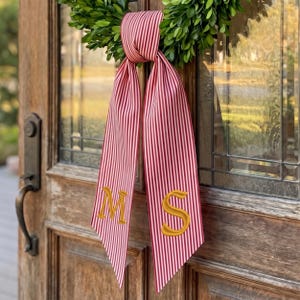 May include: A decorative ribbon featuring a red and white vertical striped pattern, tied in a knot at the top. The two long, hanging ends of the ribbon are embroidered with the gold-colored capital letters M and S, respectively.