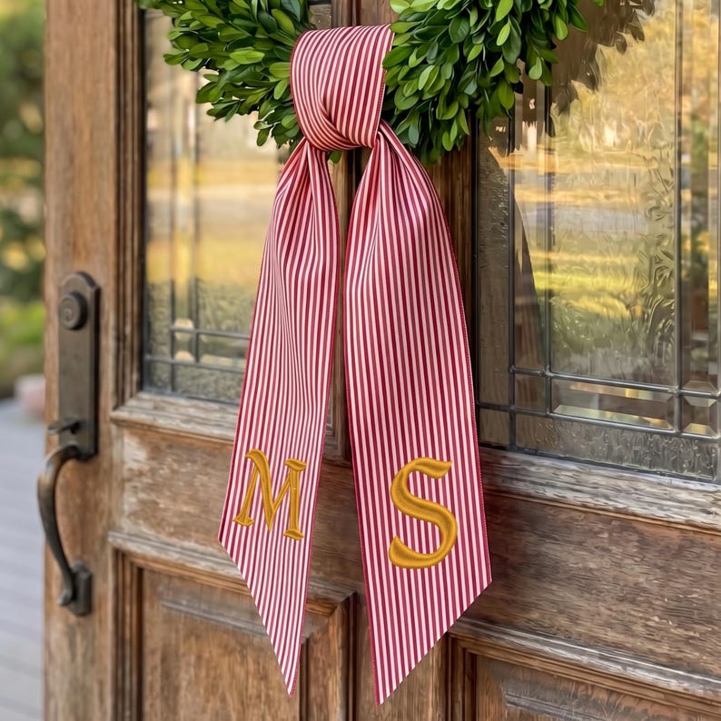 May include: A decorative ribbon featuring a red and white vertical striped pattern, tied in a knot at the top. The two long, hanging ends of the ribbon are embroidered with the gold-colored capital letters M and S, respectively.