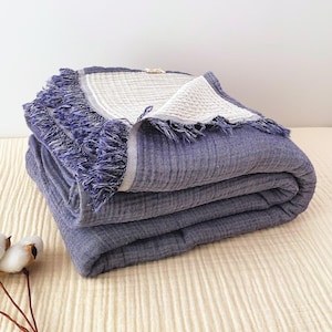 May include: A folded, blue blanket with a fringed edge. The blanket has a textured appearance and a lighter-coloured border. The blanket is stacked on top of each other. The blanket is made of a soft material.
