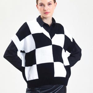 Peut inclure: Un pull sans manches à carreaux noirs et blancs avec un col en V. Le gilet est porté sur une chemise noire à col et associé à une jupe en cuir noire. Le motif du pull est un design audacieux et classique.