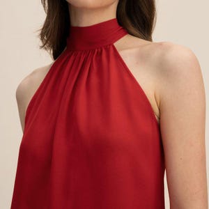 May include: A vibrant red halter top with a high neckline. The fabric drapes smoothly, creating a sleek and elegant silhouette. The top is sleeveless, showcasing the shoulders. The design is simple yet sophisticated, suitable for various occasions.